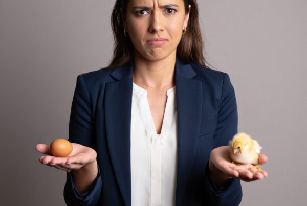 Business women holding an egg in one hand and a baby chicken in the other to represent the chicken and egg dilema of getting busines coaching when cashflow is tight